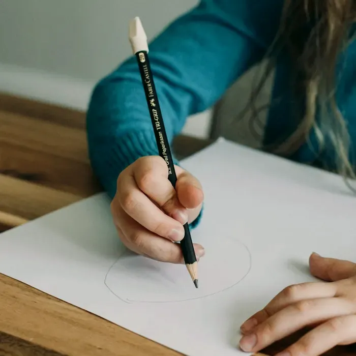 Eine Kinderhand hält einen Bleistift und zeichnet einen Kreis auf ein weißes Blatt.