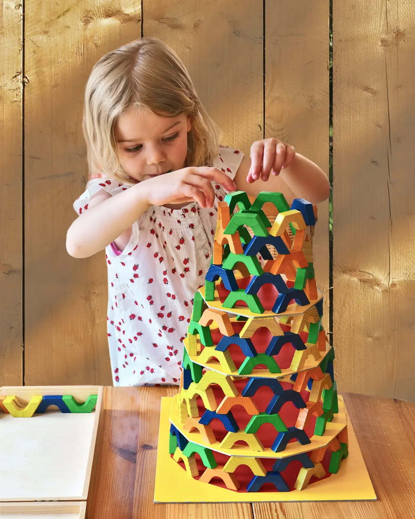 Ein Mädchen baut konzentriert einen hohen Turm aus bunten Holzbögen.